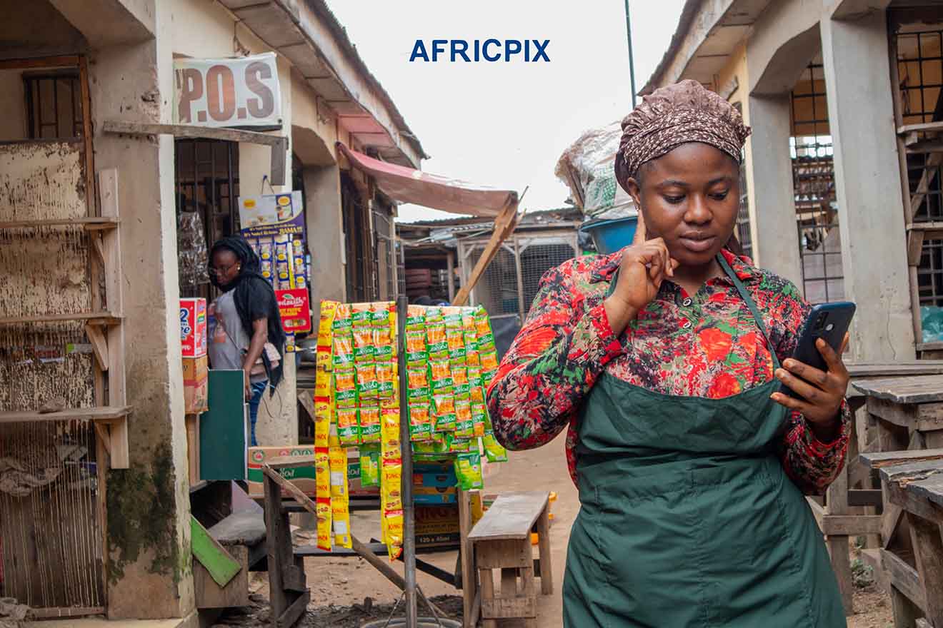 Contemplative African Market Woman Holding Phone in Front of Her Shop